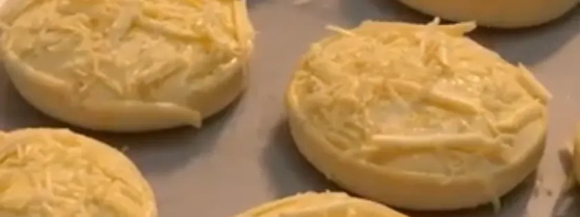 Pães de queijo com queijo ralado por cima, prontos pra assar