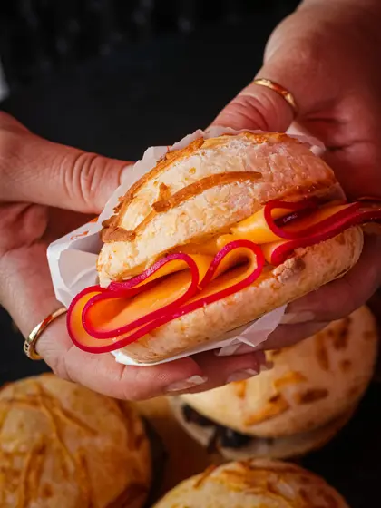 Mãos segurando um pão de queijo recheado com queijo derretido