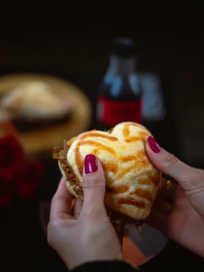Pão de queijo recheado em formato de coração nas mãos, mesa decorada